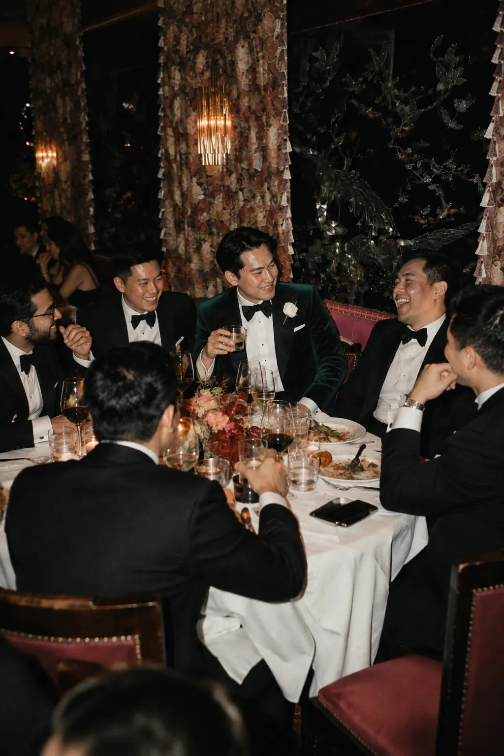 Groom and groomsmen in black tuxedos celebrating at a wedding banquet