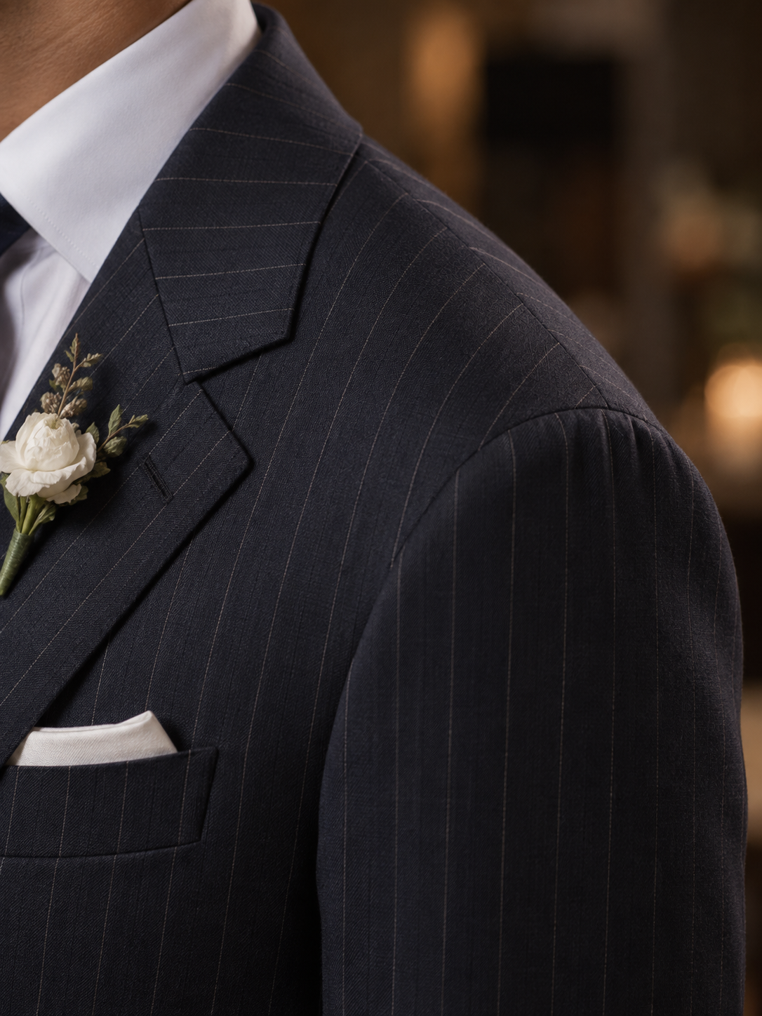 Close-up of a man wearing a dark navy pinstripe suit jacket with a white dress shirt, white pocket square, and a white rose boutonniere.